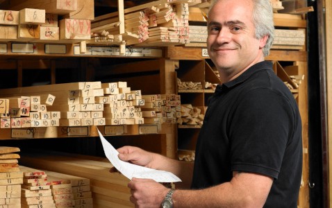 Man holding paper by planks of wood on shelves, smiling, portrai