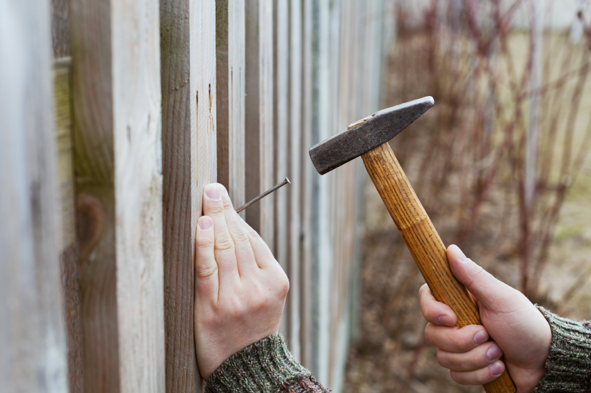 man hands drive nail with a hammer in wooden fence, carpentry